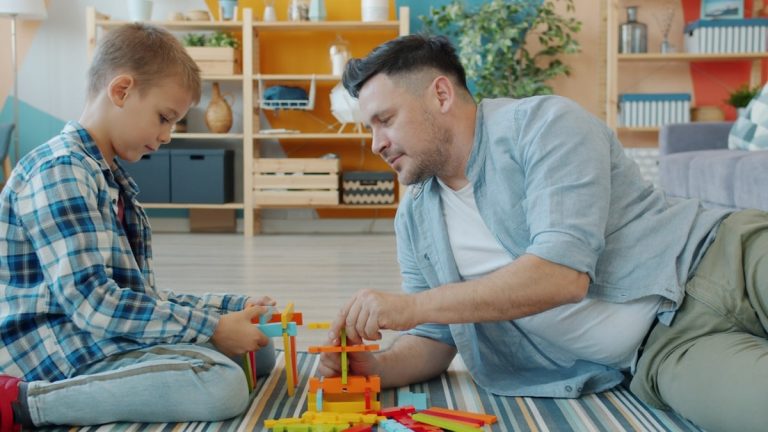 Happy family father and child are playing with bright toys at home sitting on floor together using construction blocks. Childhood, playthings and house concept.
